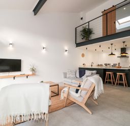 A living room with chairs and sofa facing a wall-mounted TV in an open plan space with a kitchen and dining area at Linden Barn in Wincanton