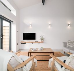 A living room with two armchairs facing a coffee table and TV mounted on the wall at Linden Barn in Wincanton