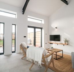A living room with wooden chairs, coffee table, wall-mounted tv, and large windows at Linden Barn in Wincanton