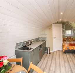 A compact living space with a kitchenette, dining table with flowers, bed, and sofa at Cherry Pod 2 in Hookagate near Meole Brace