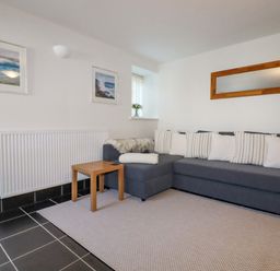 A sitting area with a gray sectional sofa and white pillows a wooden side table a wall mirror and framed pictures at The Mill in Trethevy near Tintagel