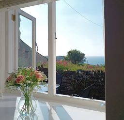 A vase with flowers on a table near an open window showing a garden wall and sea view at The Mill in Trethevy near Tintagel