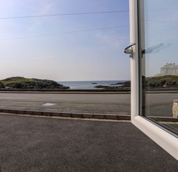 An open door showing a view of a road grassy rocky coastline and the sea at Porth Ewyn in Trearddur Bay