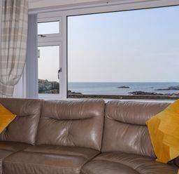 A living room with a brown leather sofa yellow cushions and a window showing a sea view at Porth Ewyn in Trearddur Bay
