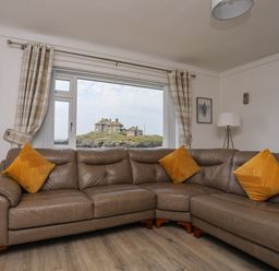 A living room with a brown leather corner sofa and yellow cushions a floor lamp checked curtains and framed pictures on the wall at Porth Ewyn in Trearddur Bay