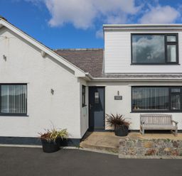 A white house with black framed windows a bench and potted plants at Porth Ewyn in Trearddur Bay