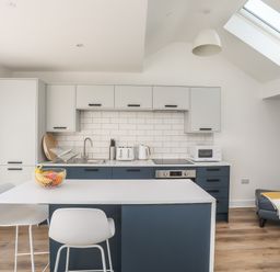 A modern kitchen with blue and white cabinets a countertop with stools and a fruit bowl at Golygfa'r Gastell Castle View in Criccieth