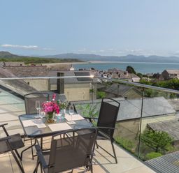 A balcony with a table and four chairs overlooking rooftops and a coastal landscape at Golygfa'r Gastell Castle View in Criccieth