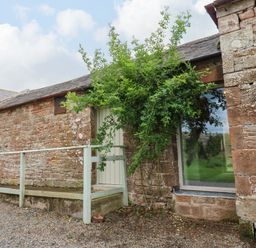 Exterior view of a stone building with a wooden door and a large window next to a tree at The Courtyard in Kirklinton near Longtown