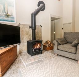 A living room with a wood burning stove gray armchair television and wooden chest at The Courtyard Kirklinton near Longtown