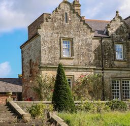 An exterior view of an old stone building with decorative gables surrounded by bushes and steps at The Pavillion in Kirklinton near Longtown