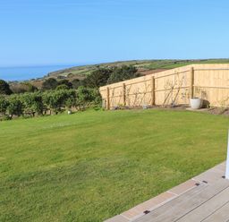 A backyard with grass a wooden fence and a view of the ocean at Greenside Studio in Praa Sands