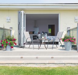 A patio with two chairs and a table with wine glasses outside a house with open doors at Greenside Studio in Praa Sands