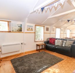 A living room with a black sofa a wooden side table a television and bunting across the ceiling at Suzanne's Beach Hut in Bacton near Walcott