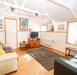 A living room with two sofas a TV on a wooden stand a gray rug and wall art at Suzannes Beach Hut in Bacton near Walcott