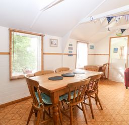 A dining room with a wooden table and six chairs two windows and a red armchair at Suzanne's Beach Hut in Bacton near Walcott