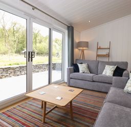 A living room with two gray sofas a wooden coffee table a striped rug a floor lamp and sliding glass doors at Hawthorn Croft in Haverthwaite