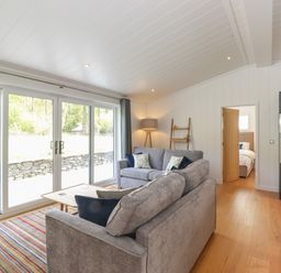 A living room with two grey sofas a striped rug a wooden coffee table large windows and an open door to a bedroom at Hawthorn Croft in Haverthwaite