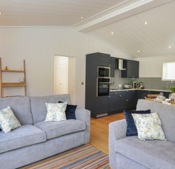 A living area with two grey sofas with cushions a kitchen with dark cabinets and a dining table at Hawthorn Croft in Haverthwaite