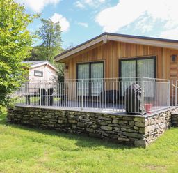 A wooden cabin with a stone foundation and metal railing on a grassy lawn at Ash Thwaite in Haverthwaite