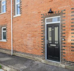 A black front door with the number 6 on a brick house with two windows at The Corner House in Weymouth