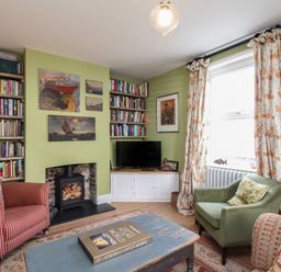 A living room with bookshelves a fireplace armchairs and a window with floral curtains at The Corner House in Weymouth