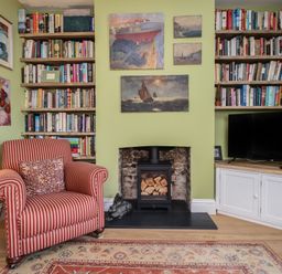 A sitting area with a striped armchair a fireplace with stacked firewood bookshelves and a television cabinet at The Corner House Weymouth