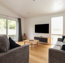 A living room with two grey sofas a wooden coffee table a wall-mounted television and large windows with grey curtains at The Brambles in Haverthwaite