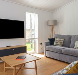 A living room with a grey sofa a wooden coffee table and a mounted television at The Brambles in Haverthwaite