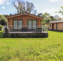 A wooden cabin with a stone base and metal railing on a porch in a grassy area at The Brambles in Haverthwaite