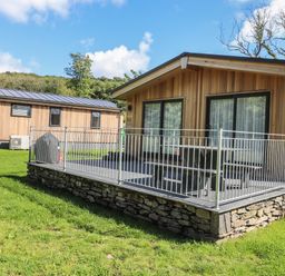 A wooden cabin with a fenced stone patio and outdoor furniture in a grassy area at The Burrow in Haverthwaite
