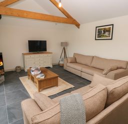 A living room with sofas a wooden coffee table a fireplace and a television at The Byre in St Brides Major