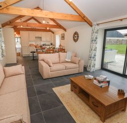 A living room with beige sofas wooden coffee table and sliding glass doors overlooking a garden at The Byre in St Brides Major