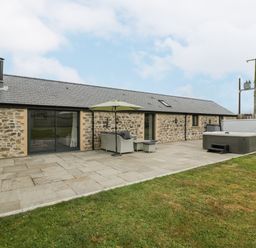 An outdoor patio area with stone flooring a hot tub seating with umbrella and a stone building at The Byre in St Brides Major