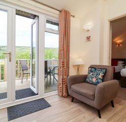 A living area with an armchair and door leading to a balcony with chairs and table at Chalet Log Cabin C11 in Combe Martin