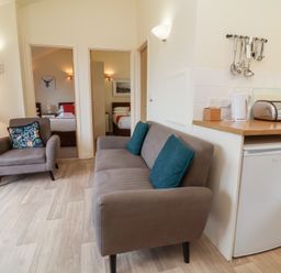 A living room with a grey sofa and chair near two doorways leading to bedrooms at Chalet Log Cabin C11 in Combe Martin
