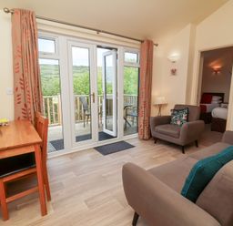 A living room with chairs a table and glass doors leading to a balcony at Chalet Log Cabin C11 in Combe Martin