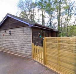 A stone and wood cabin with a wooden fence and gate surrounded by trees at Chalet Log Cabin C9 in Combe Martin