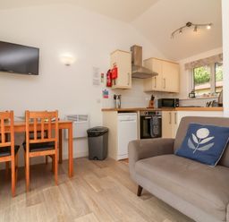 A kitchen with wooden dining table and chairs a gray sofa and a wall mounted television at Chalet Log Cabin C9 in Combe Martin