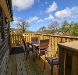 A wooden balcony with a table and four chairs overlooking trees and hills at Chalet Log Cabin L3 in Combe Martin