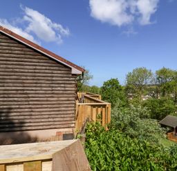A wooden log cabin with a wooden deck overlooking trees and a nearby cabin at Chalet Log Cabin L3 Combe Martin