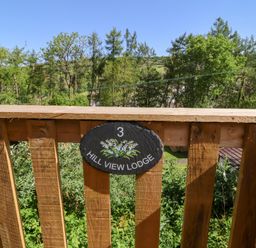 A wooden balcony railing with a sign reading 3 Hill View Lodge with trees and hills in the background at Chalet Log Cabin L3 in Combe Martin