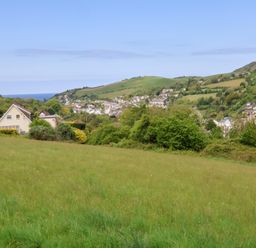 A grassy field with houses and hills in the background at Chalet Log Cabin L3 in Combe Martin