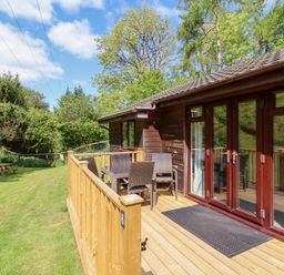A wooden deck with a table and four chairs outside a wooden cabin in a grassy area with trees at Chalet Log Cabin L6 in Combe Martin