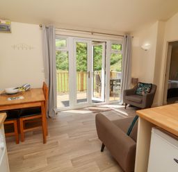 A living room with a wooden dining table and chairs a mounted television and armchairs next to glass doors leading to a deck at Chalet Log Cabin L6 in Combe Martin