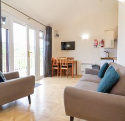 A living room with two sofas a wooden dining table with chairs and a wall mounted TV at Chalet Log Cabin L10 in Combe Martin