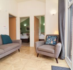 A sitting area with a sofa and armchair facing two open doors showing bedrooms at Chalet Log Cabin L10 in Combe Martin