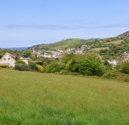 A grassy field with houses and trees in the background near hills and a body of water at Chalet Log Cabin L12 in Combe Martin