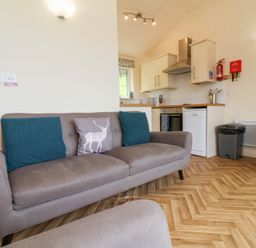 A living area with a grey sofa with cushions next to a kitchen with white cabinets and appliances at Chalet Log Cabin L14 in Combe Martin