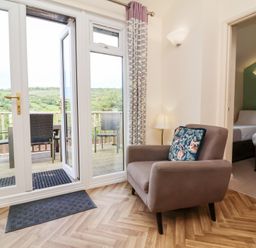 A living area with an armchair and glass doors opening to a balcony with chairs at Chalet Log Cabin L14 in Combe Martin